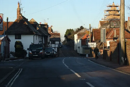 Escena callejera en Ditchling con casas, coches y cartel de pub.