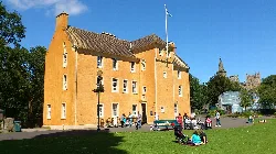 A yellow historic house with people sitting and walking nearby in a park.