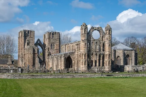 Ruins of Elgin Cathedral with tall stone walls and arches, under a partly cloudy sky.