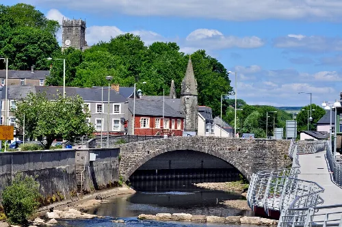 Puente de piedra con dos torres y pasarela sobre un río en Bridgend.