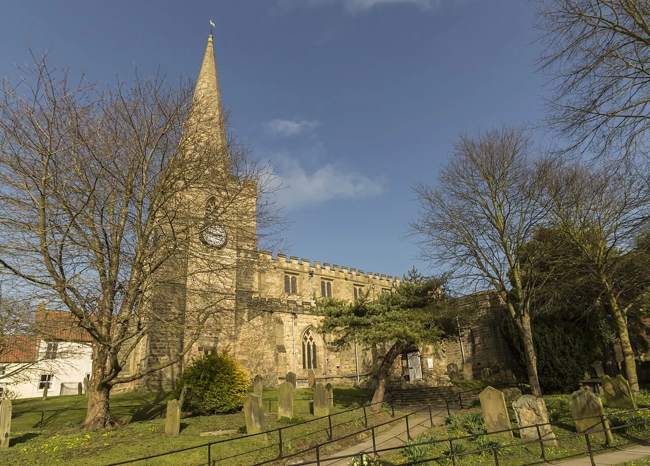 Iglesia de piedra con torre alta, árboles y lápidas en Pickering.