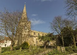 Iglesia de piedra con torre alta, árboles y lápidas en Pickering.