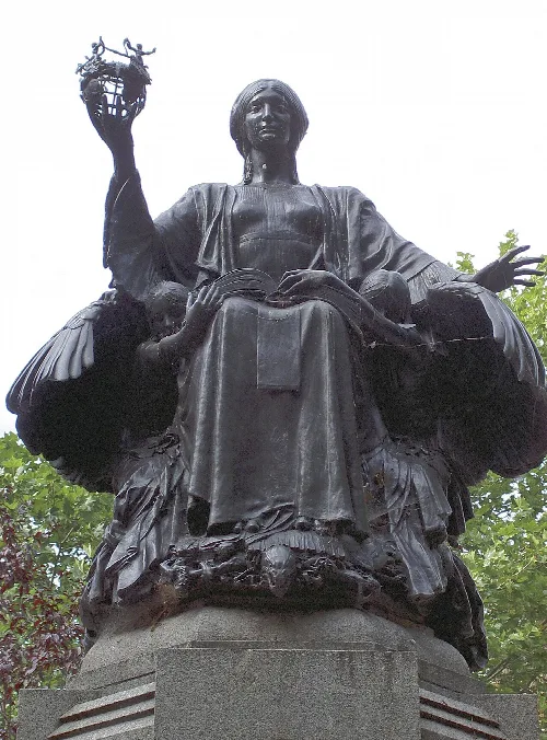 A dark metal angel statue holding a book and a crown.