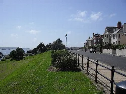 Vista de The Rath, césped verde, arbustos y casas junto al agua.