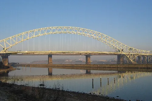 Eine große Bogenbrücke über einem Fluss mit Fabriken im Hintergrund.