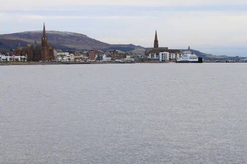 View of the waterfront in Largs with churches and a ferry.