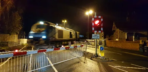 Tren pasando por Haxby Gates de noche, barreras y señales de advertencia.