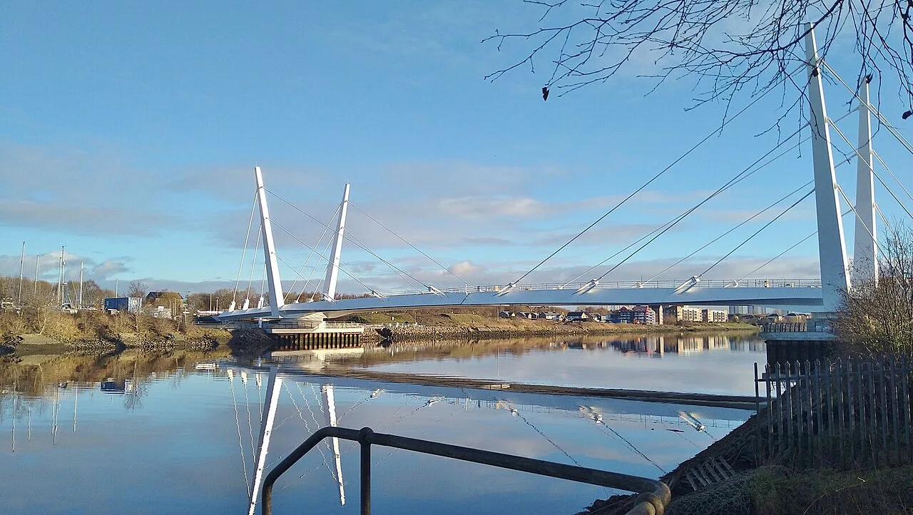 Eine Brücke mit Seilen über einem Fluss unter blauem Himmel.