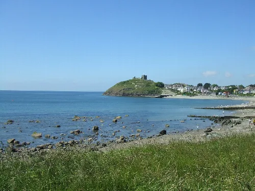 Vista del castillo de Criccieth en una colina sobre la playa y el pueblo, con césped y mar tranquilo.