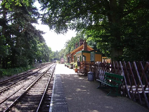View of Holt Railway station with train tracks, benches, and a small station building.