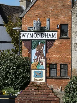 Cartel de Wymondham con escena pintada y figura en la parte superior.