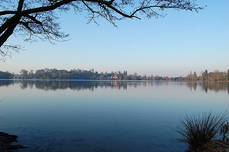 Agua tranquila con árboles y pueblo al fondo en Ellesmere.