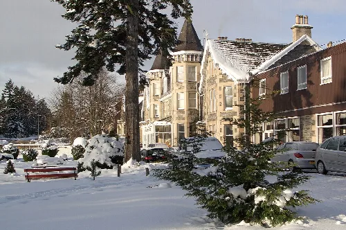 Verschneite Gebäude, Bäume und Autos in Grantown-on-Spey im Winter.