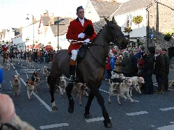 Hombre con abrigo rojo montando un caballo con perros y espectadores en Cowbridge.