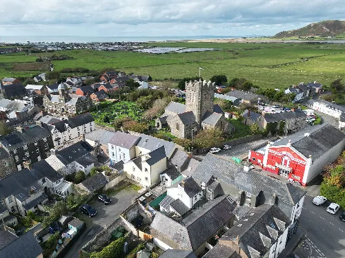 Vista aérea de Tywyn con iglesia y casas, campos verdes y costa.