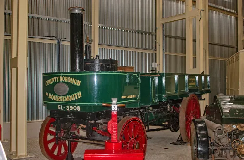 Green steam lorry with red wheels and black chimney in a museum.