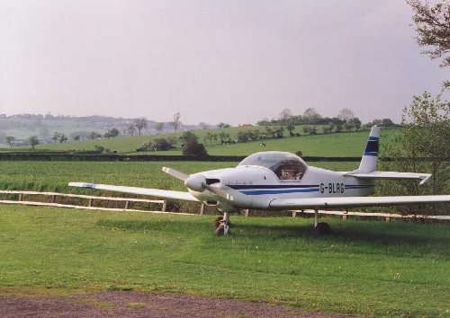 Un avión pequeño blanco con rayas azules en césped con campos en el fondo.