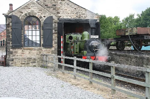 Grünes Tanklokomotive fährt aus einem Steingebäude im Shildon Railway Museum.