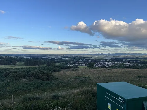 Aussicht auf Westhill mit Häusern, Feldern und bewölktem Himmel.