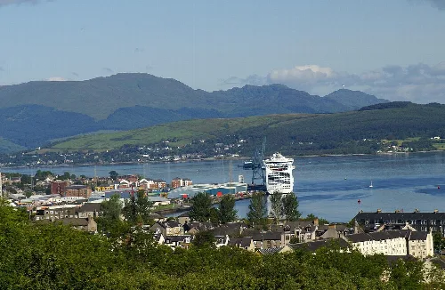 Panoramic view of Greenock with a cruise ship at the dock and mountains in the background.