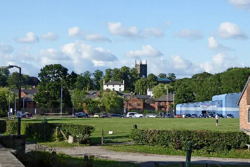 Park with green grass, trees, and a church tower in the distance.