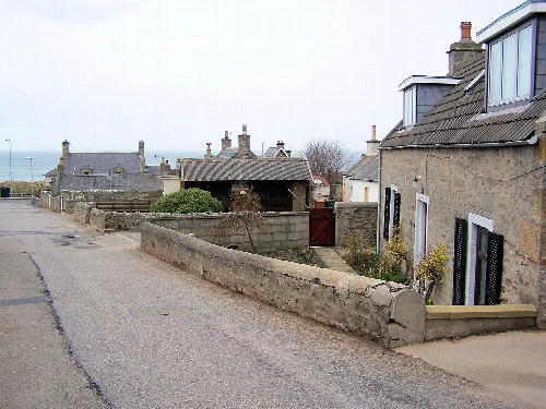 Stone houses with chimneys and a stone wall along the street in Lossiemouth.