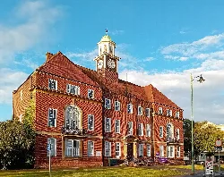 Red brick town hall with a clock tower and a red roof.