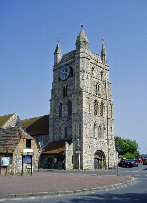 Stone church tower with a clock and four spires in New Romney.