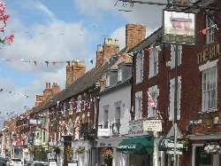 View of High Street with brick buildings and pub signs for the Bull and the Cock.
