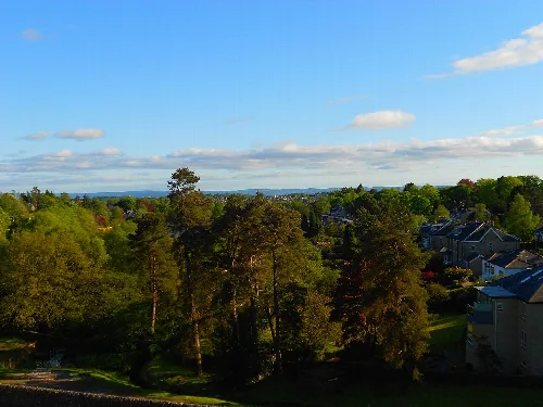 Bäume und Häuser in Milngavie unter einem bewölkten Himmel.