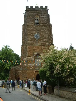 Steinerne Kirchturm mit Menschenmenge und buntem Girlanden.