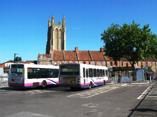 Two buses at Wells bus station with St Cuthbert's church tower behind.
