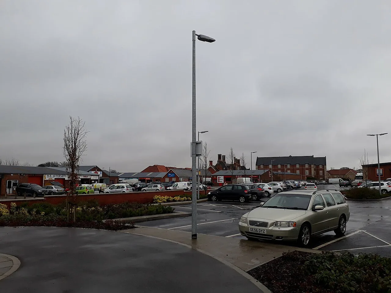 Estacionamiento con coches y edificios industriales al fondo.