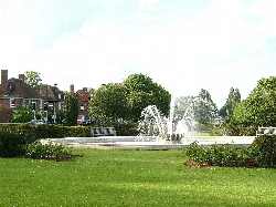 Fuente con chorros de agua en un parque rodeado de árboles y casas.