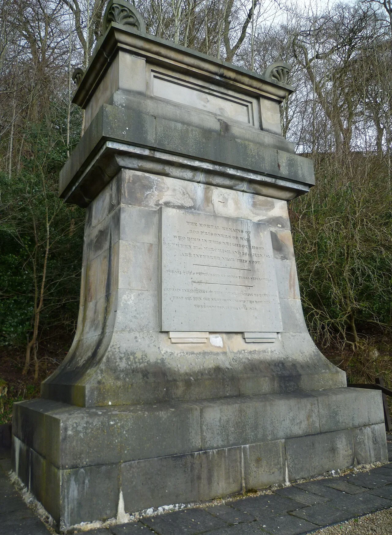 Monumento de piedra con inscripción, rodeado de árboles en Penicuik.