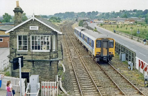 Caseta de señal y tren en la estación de Malton con vías y puente peatonal.