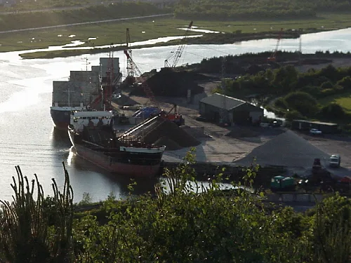 Barcos, grúas y pilas de chatarra en un astillero.