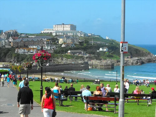 People sitting on benches and walking on a grassy area near the beach in Newquay.