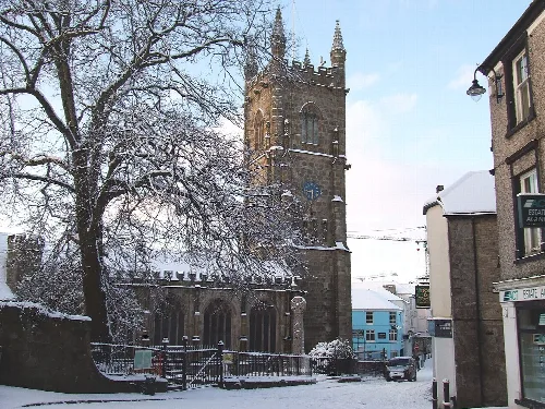 Snow-covered church with a tall stone tower and trees in St Austell.