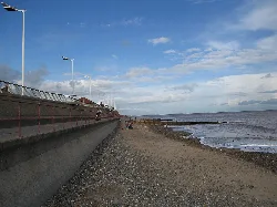 Vista de la playa de Hornsea con paseo, piedras y mar bajo un cielo azul.