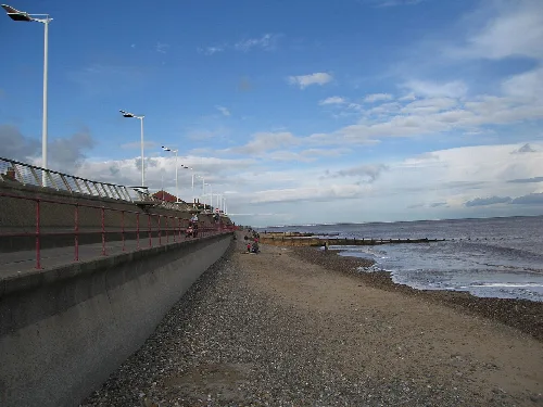 View of Hornsea beach with promenade, pebbles, and sea under a blue sky.