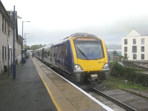 A blue and yellow train at Kendal Station on the platform.