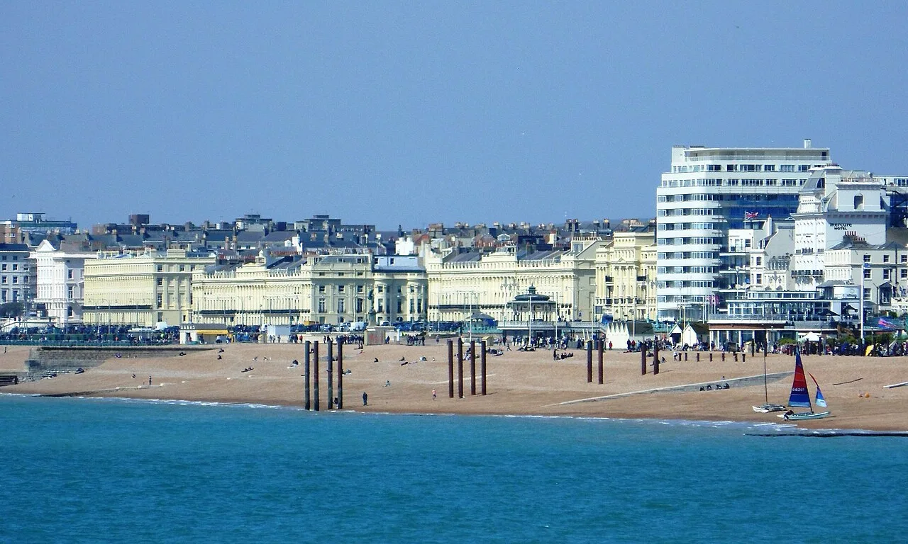 Edificios del paseo marítimo desde el Palace Pier, con playa y velero en primer plano.