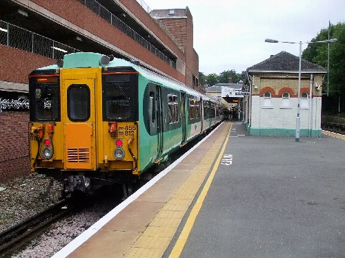 A green and yellow train at a station platform with a small building nearby.