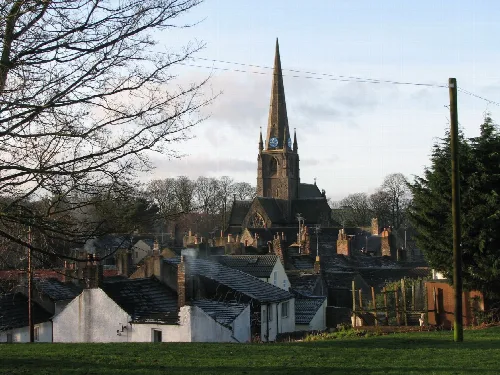 Kirche mit hohem Turm in Cockermouth, Cumbria, umgeben von Dächern und Bäumen.