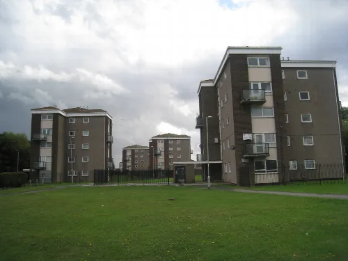 Multiple apartment buildings with balconies and a grassy area in front.