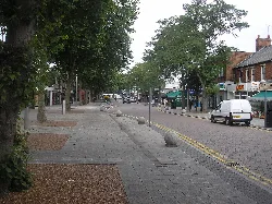 Straßenszene mit Geschäften, Bäumen und parkenden Autos in Bletchley.