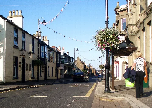 View of Carnoustie High Street with shops, a woman walking, and hanging bunting.