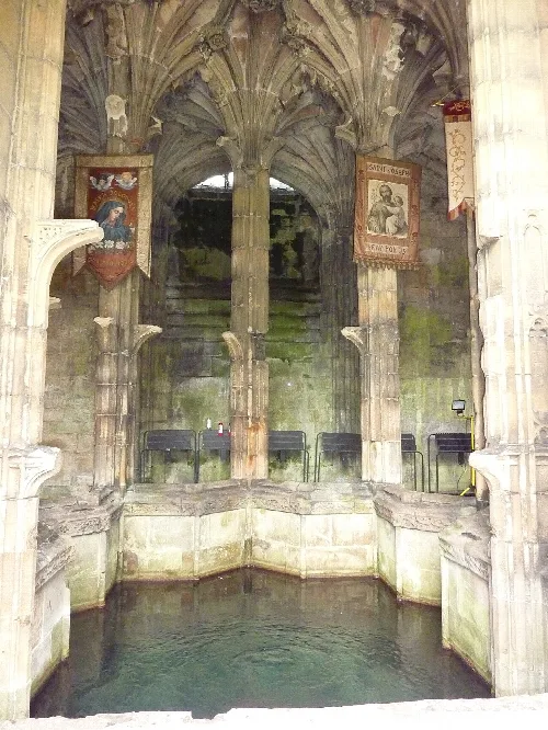 Estructura de piedra con lavabo de agua, arcos góticos y banderas religiosas.