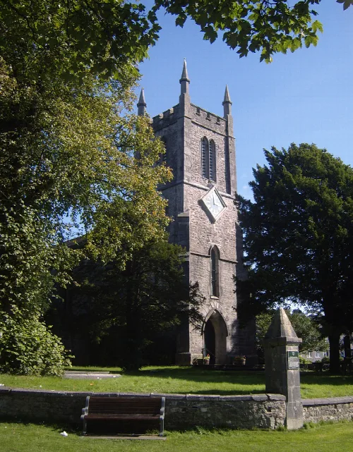 Stone church tower with clock, surrounded by trees and a clear blue sky.